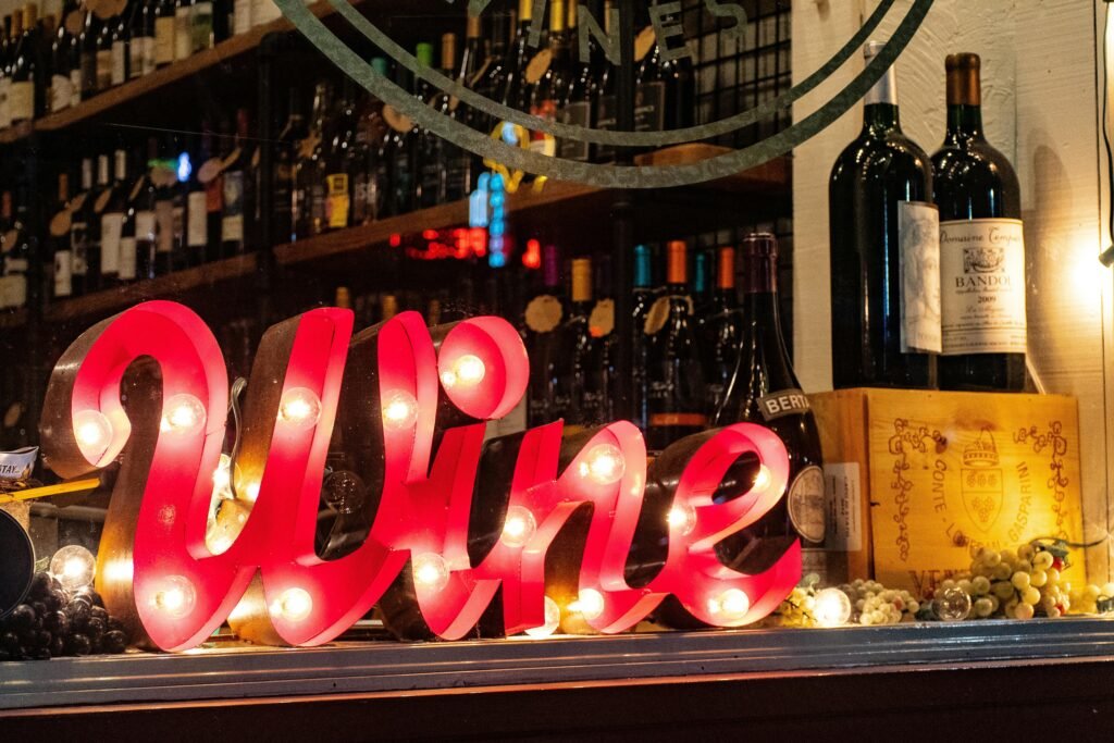 Illuminated wine sign with bottles and grapes create a lively ambiance in a liquor store window.